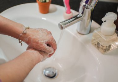 Açık tenli Asyalı kadın banyo lavabosunda köpüklü ellerini sabunla yıkıyor. Virüs ya da bakteriyel yayılma önleme için hijyen ve temizliği gösterir