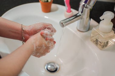 Açık tenli Asyalı kadın banyo lavabosunda köpüklü ellerini sabunla yıkıyor. Virüs ya da bakteriyel yayılma önleme için hijyen ve temizliği gösterir