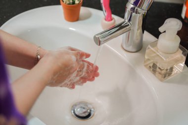 Açık tenli Asyalı kadın banyo lavabosunda köpüklü ellerini sabunla yıkıyor. Virüs ya da bakteriyel yayılma önleme için hijyen ve temizliği gösterir