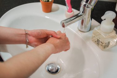 Açık tenli Asyalı kadın banyo lavabosunda köpüklü ellerini sabunla yıkıyor. Virüs ya da bakteriyel yayılma önleme için hijyen ve temizliği gösterir