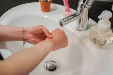 Açık tenli Asyalı kadın banyo lavabosunda köpüklü ellerini sabunla yıkıyor. Virüs ya da bakteriyel yayılma önleme için hijyen ve temizliği gösterir
