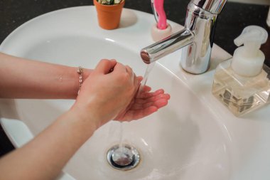 Açık tenli Asyalı kadın banyo lavabosunda köpüklü ellerini sabunla yıkıyor. Virüs ya da bakteriyel yayılma önleme için hijyen ve temizliği gösterir