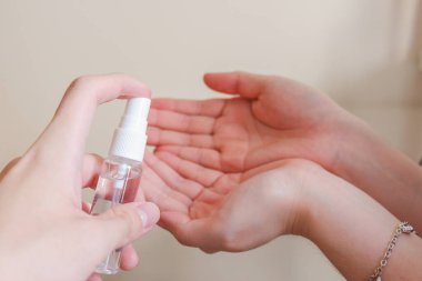 Açık tenli Asyalı bir kadın el dezenfektanı sprey şişesini başka bir ele pompalıyor. Virüs ya da bakteriyel yayılma önleme için hijyen ve temizliği gösterir