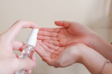 Açık tenli Asyalı bir kadın el dezenfektanı sprey şişesini başka bir ele pompalıyor. Virüs ya da bakteriyel yayılma önleme için hijyen ve temizliği gösterir