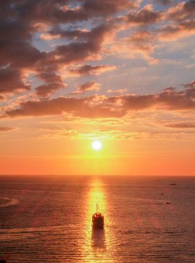 Güneşle aynı hizada olan bir yelkenli teknesi Labuan Bajo 'da bir marinayla birlikte hafif bulutlu bir gün batımında suya vuruyor.