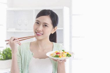 Mutfakta bir tabak sebze tutarak ve gülümseyen duran Genç Asyalı kadın