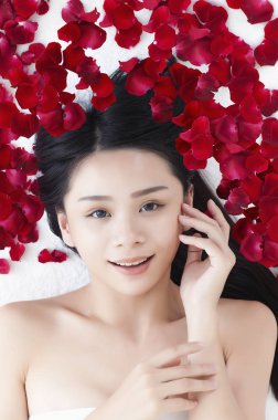 Genç Asyalı kadın başının yanında yatıp kameraya gülümsüyor.,