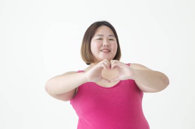 Genç şişman Asyalı kadın el ele tutuşup kalp şekli oluşturuyor ve kameraya gülümsüyor.