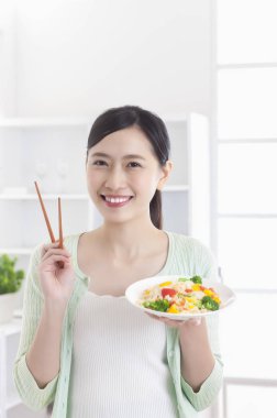 Mutfakta bir tabak sebze tutarak ve gülümseyen duran Genç Asyalı kadın