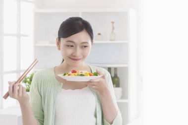 Mutfakta bir tabak sebze tutarak ve gülümseyen duran Genç Asyalı kadın