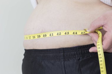 Genç şişman Asyalı adam belini ölçüyor.,