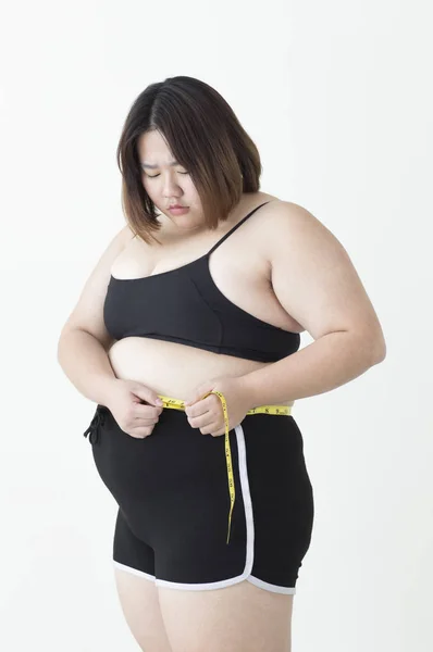 年轻的肥胖亚洲女人拿着一条测量腰围的带子 看起来很沮丧 — 图库照片