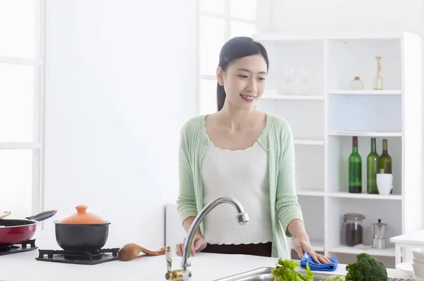 Young Asian woman standing in the kitchen smiling cleaning the kitchen