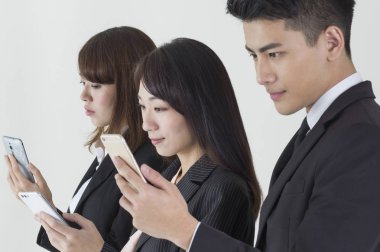 Takım elbiseli genç Asyalı erkek ve kadınlar cep telefonlarını kontrol ediyorlar.,