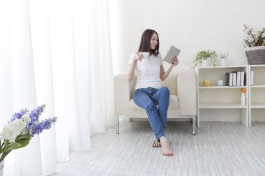 Tablet ve dizüstü bilgisayarla kanepede oturan genç kadın.