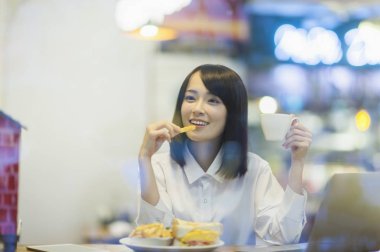 Bir öğleden sonra çay içiyor ve gülümseyen bir takım elbise giymiş genç Asyalı kadın