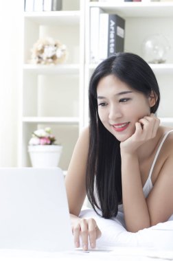 Genç kadın yatakta yatıyordu ve onu laptop kullanarak gülümseyen güzel