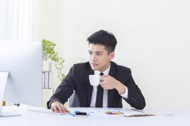 Onun bilgisayarı kullanmak ve kahve içme gülümseyen bir takım elbise giymiş genç Asyalı adam