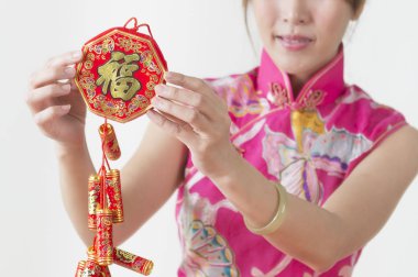 Kırmızı kestane fişeği tutarak ve gülümseyen bir kırmızı Çin geleneksel kıyafet giyen genç Çinli kadın,