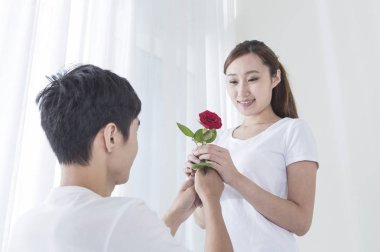 Kırmızı gül tutan ve genç bir kadın için veren genç adam