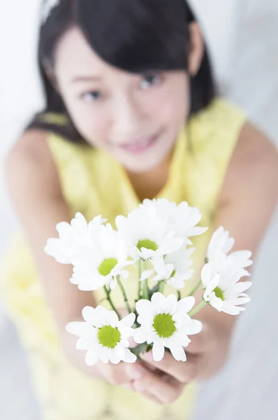 Young girl holding up a flower and smiling showing to the camera