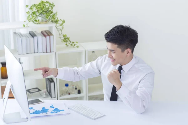 Young Asian man wearing a suit smiling pointing at his computer