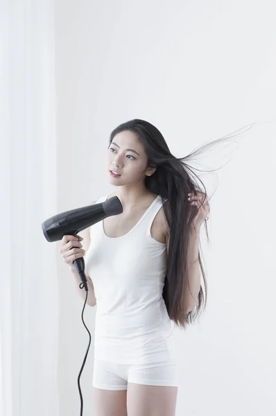 Young Asian woman drying her hair and smiling looking away
