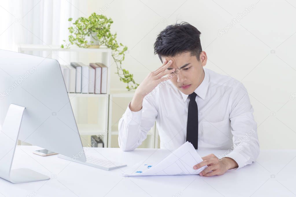 Young Asian man wearing a suit hands on his forehead looking painful