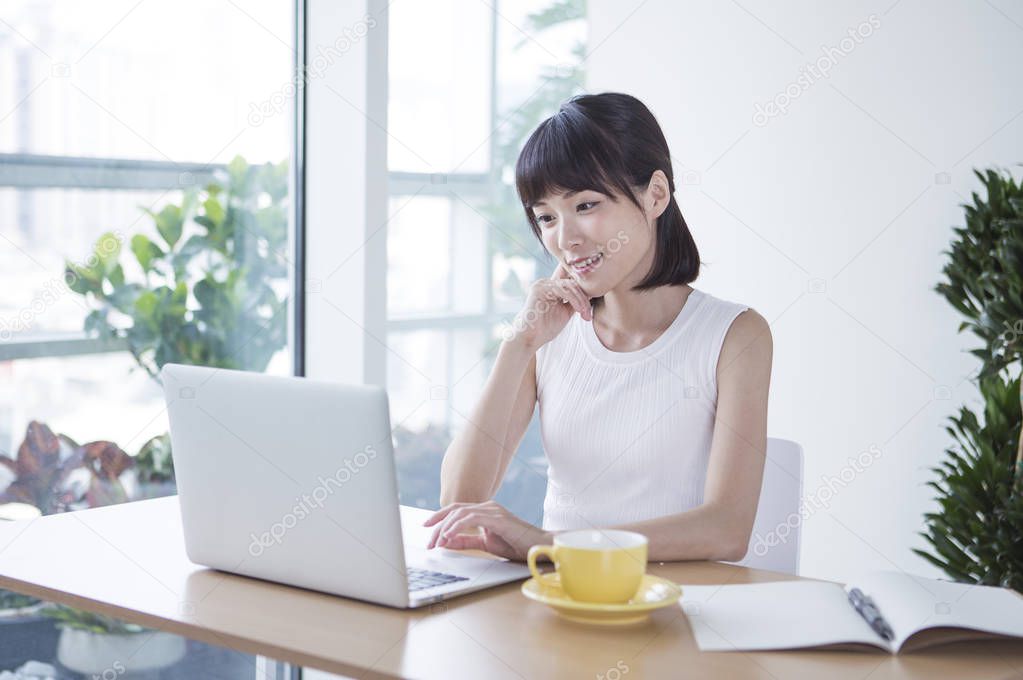 Young woman in a white suit sitting at the desk smiling working on the laptop