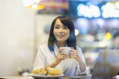 Takım elbiseli genç Asyalı kadın çay içiyor ve gülümsüyor.,