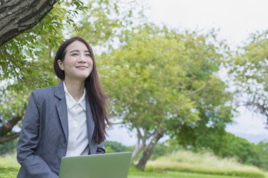 Dizüstü bilgisayar kullanarak gülümseyen bir takım elbise giyen genç Asyalı kadın