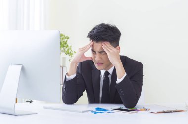 Bir takım elbise giymiş genç Asyalı adam kafasına ağrılı seyir eller