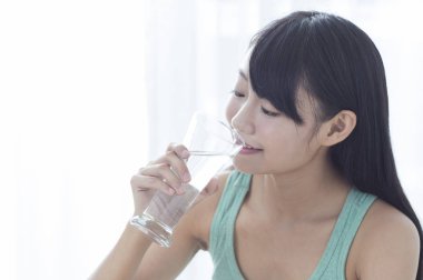 Bir bardak su tutarak ve gözleriyle gülümseyen genç kız kapalı