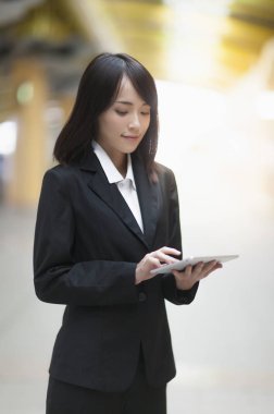 Onun tablet kullanarak gülümseyen bir takım elbise giyen genç Asyalı kadın