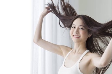 Young Asian woman hands playing with her hair and smiling at the camera clipart