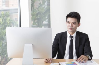 Masada oturan ve onun bilgisayar üzerinde çalışmaya gülümseyen elbiseli Genç adam