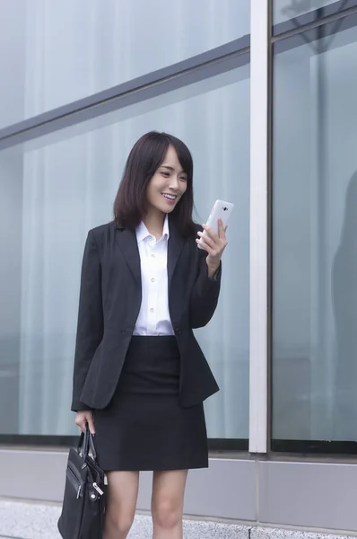 Young Asian woman in a suit holding a suit case and smiling looking at her mobile phone