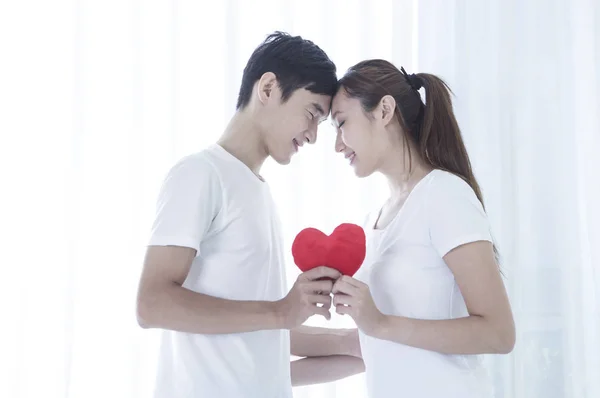 Young couple holding a heart and heads together and smiling to each other