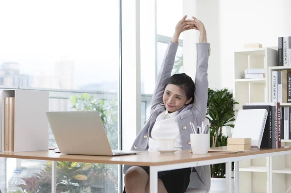 Young woman in a suit sitting at the table and stretching