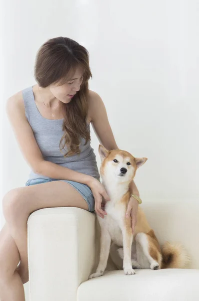 身穿蓝色衣服的年轻亚洲女人坐在沙发上笑着抱着她的狗 — 图库照片