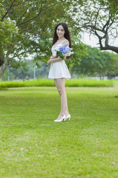 穿着白色礼服的年轻亚洲女人拿着一朵花 对着镜头微笑 — 图库照片