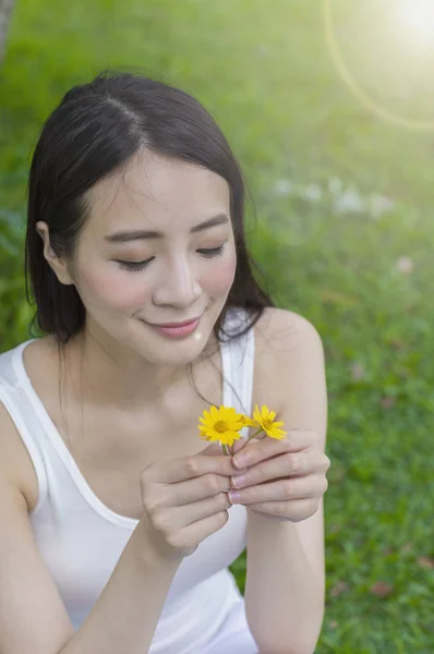 Young Asian woman holding a flower and smiling looking at it
