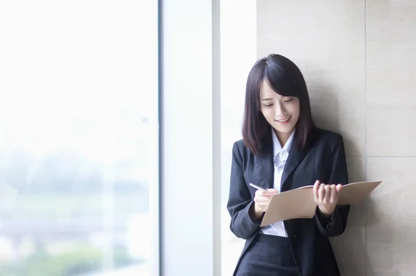 Young Asian woman in a suit writing and smiling,