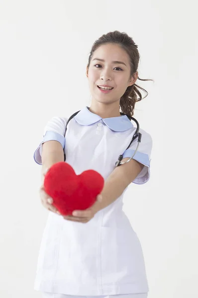 年轻的护士抱着一颗心 对着摄像机微笑 — 图库照片