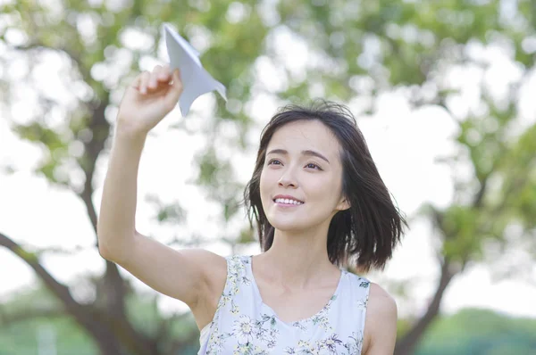 紙飛行機を押しながらよそ見を笑顔の若いアジア女性 — ストック写真