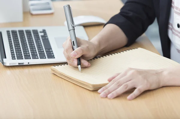 Young woman in a suit sitting at the table and taking a note