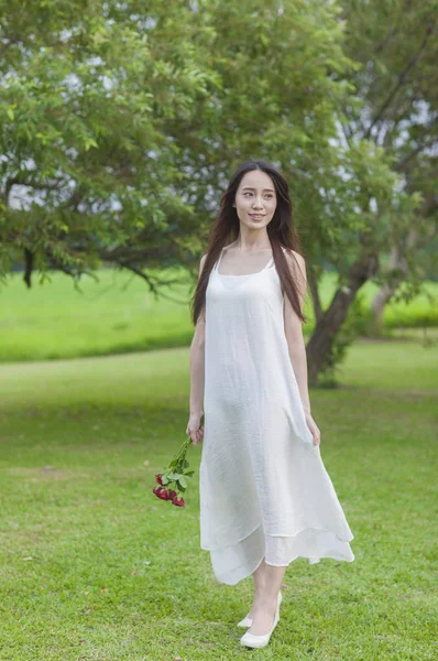 穿着白色礼服的年轻亚洲女人拿着一朵花 对着镜头微笑 — 图库照片