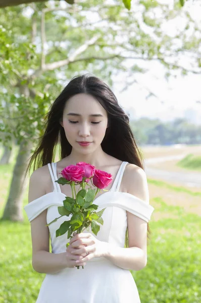 穿着白色礼服的年轻亚洲女人拿着一朵花 面带微笑 — 图库照片