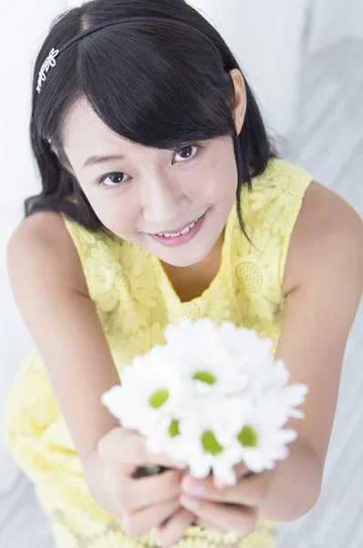 Young girl holding up a flower and smiling showing to the camera