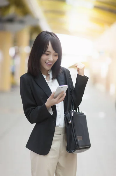 Young Asian woman in a suit smiling at her mobile phone